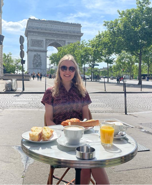 Carina sitting at a table in Paris enjoying breakfast outside