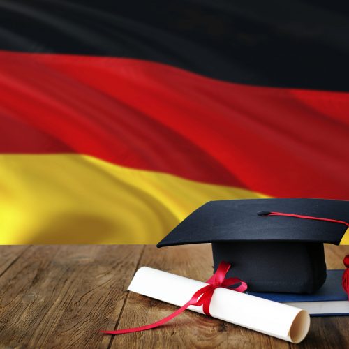 Germany education concept. Graduation cap and diploma on wooden table, national flag background. Succesful student.