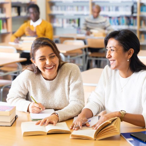 Two young adult women gaining new skills at public library, reading books and making notes